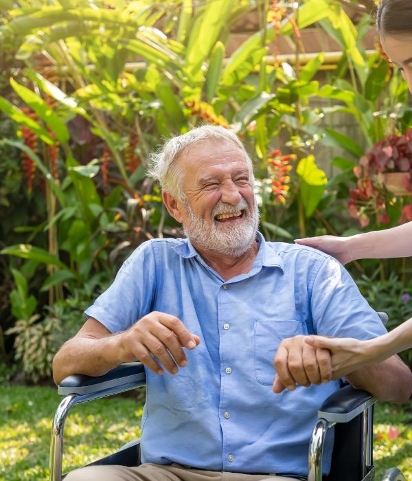 Caregiver supporting an older man in a wheelchair during personal care.
