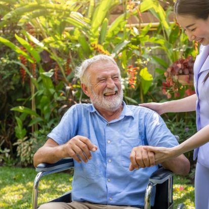 Caregiver supporting an older man in a wheelchair during personal care.