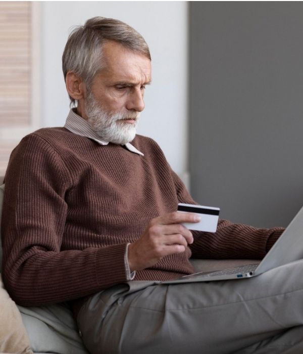 Older man looking for Molicare products sitting on a sofa and shopping online using a laptop.