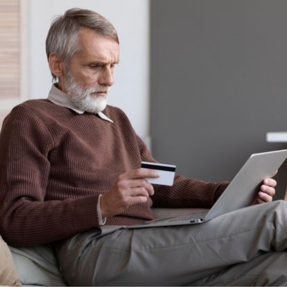 Older man looking for MoliCare® products online while sitting on a sofa with a laptop.