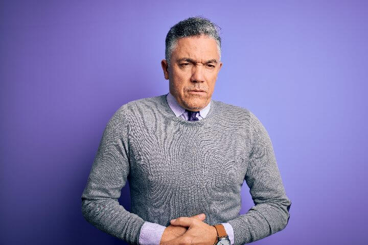 greyhaired man with hand on stomach with constipation and urinary incontinence
