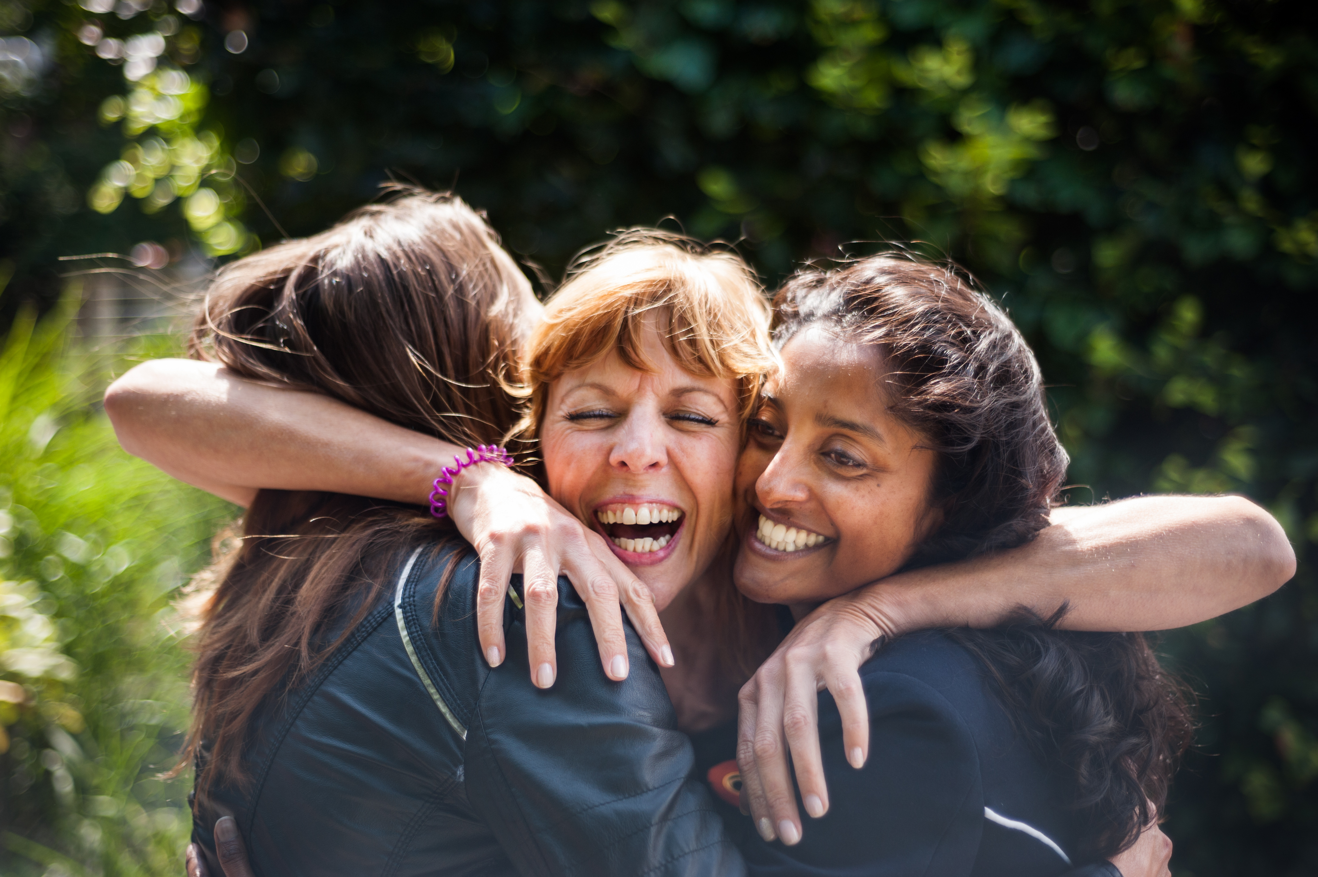 Three middle-aged women embrace each other and laugh together.